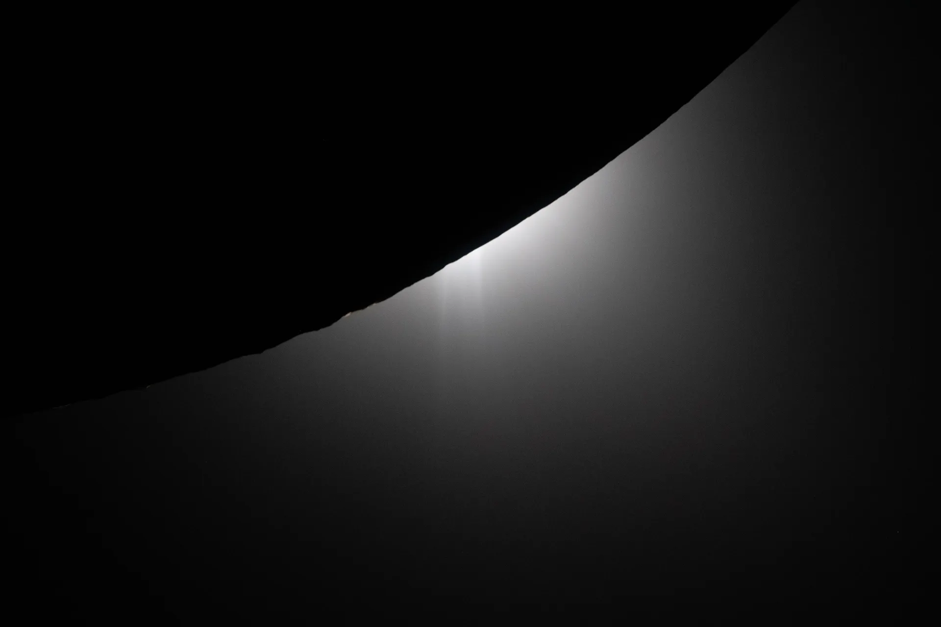The black limb of the Moon cuts across the frame as a bright glow of sunlight spreads from behind it.