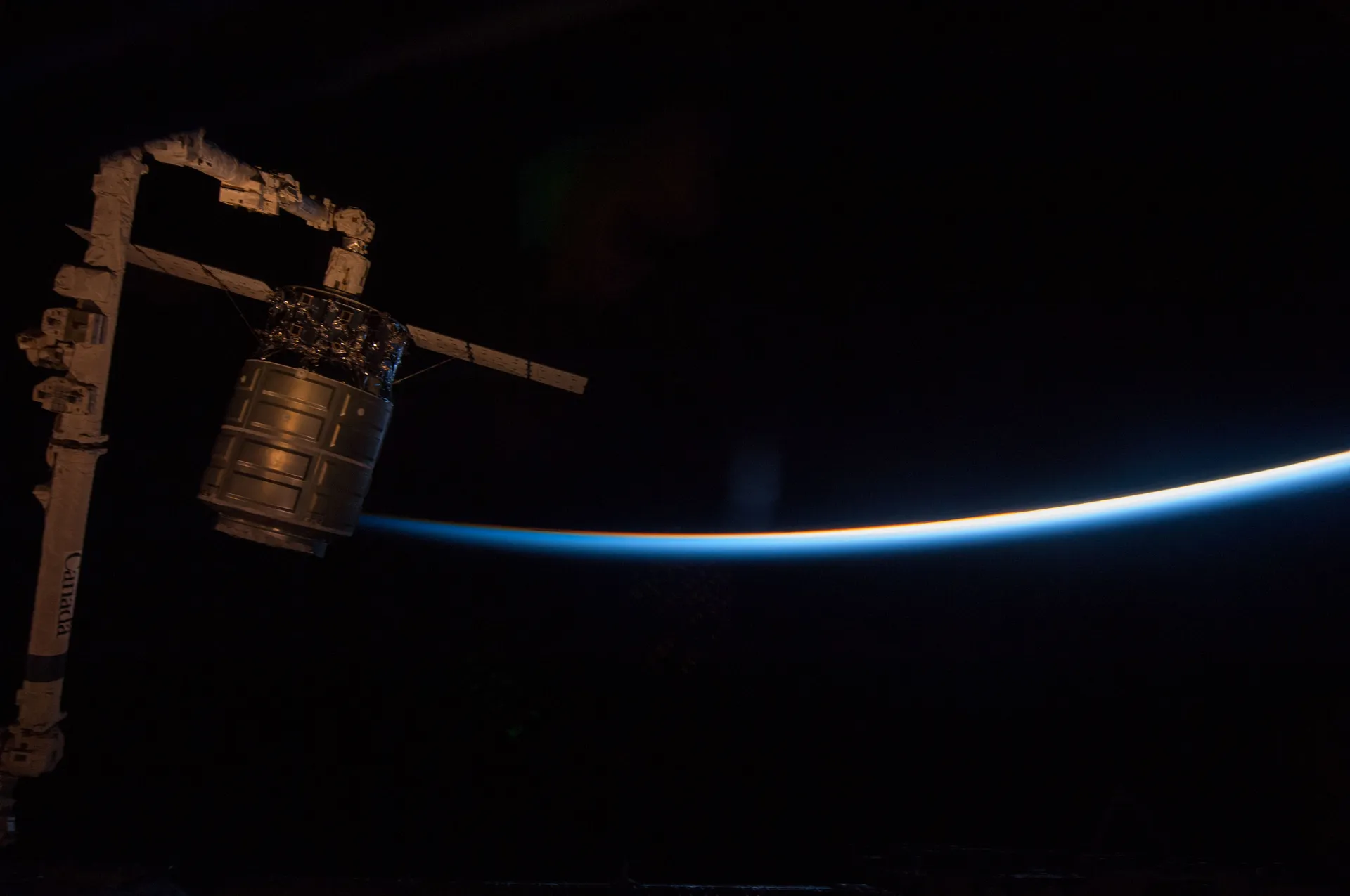 The first Cygnus cargo spacecraft held by the station’s robotic arm against black space and the thin blue line of the atmosphere.