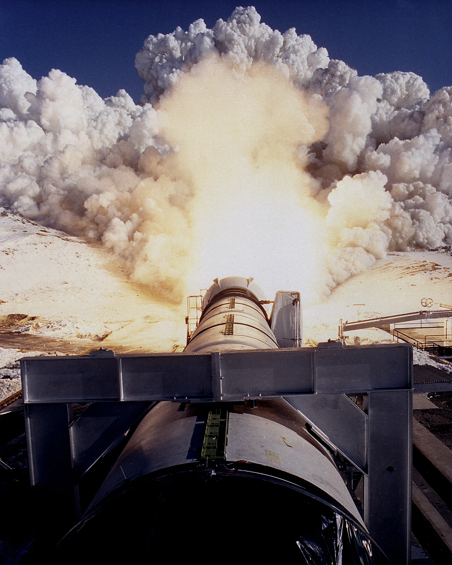 A horizontal solid rocket motor fires during a ground test, throwing up a huge cloud.