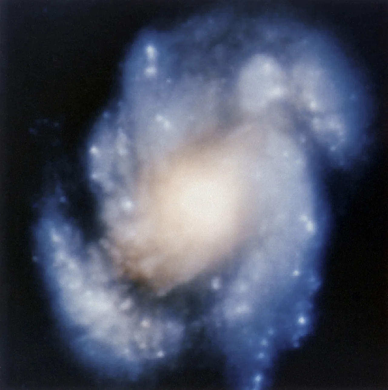 A soft, blurred spiral of blue and cream light: the core of galaxy M100 as seen through Hubble’s flawed optics.