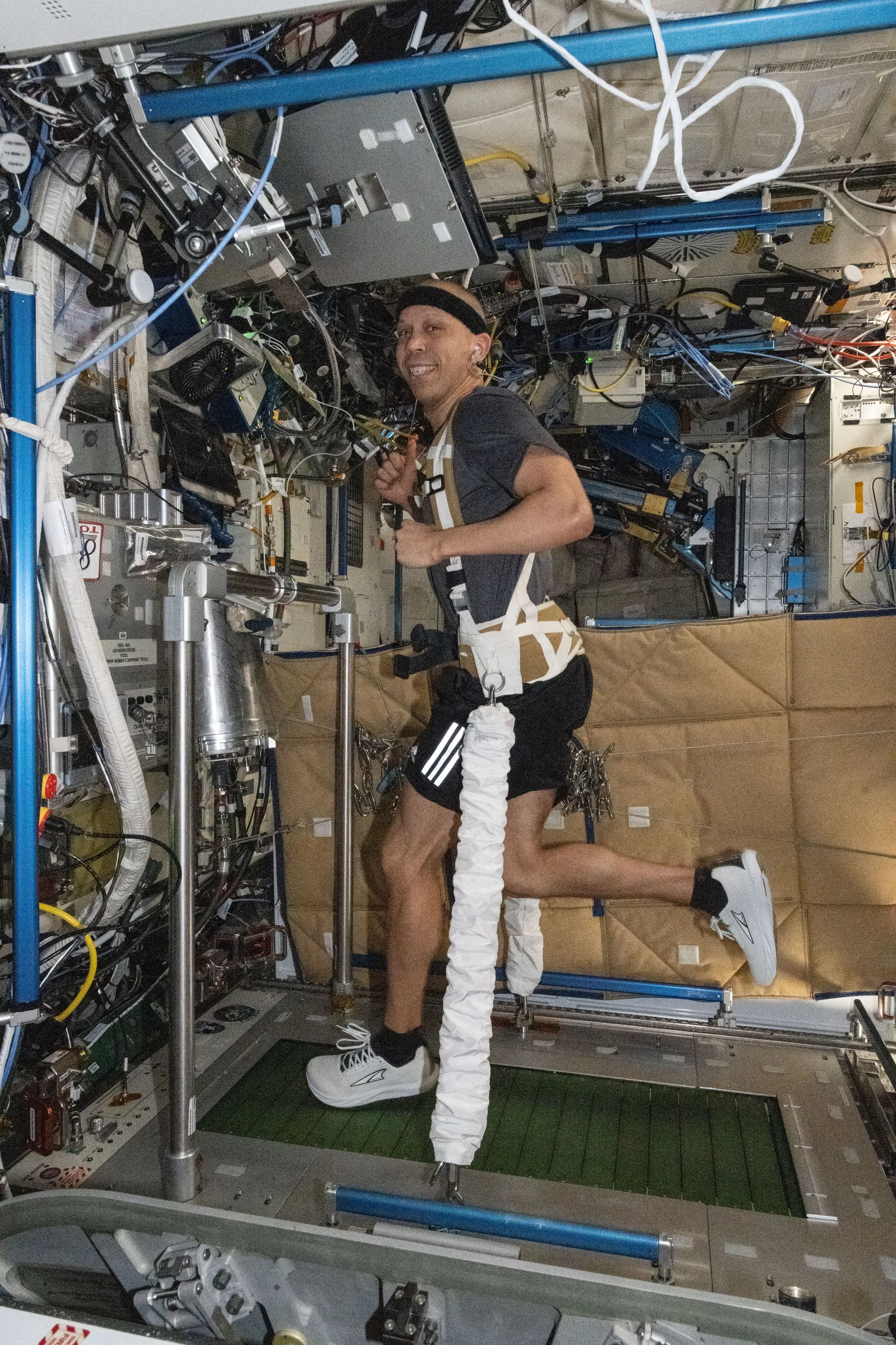 Chris Williams runs on a treadmill set into the floor of the Tranquility module, held down by a harness and white bungee cords.
