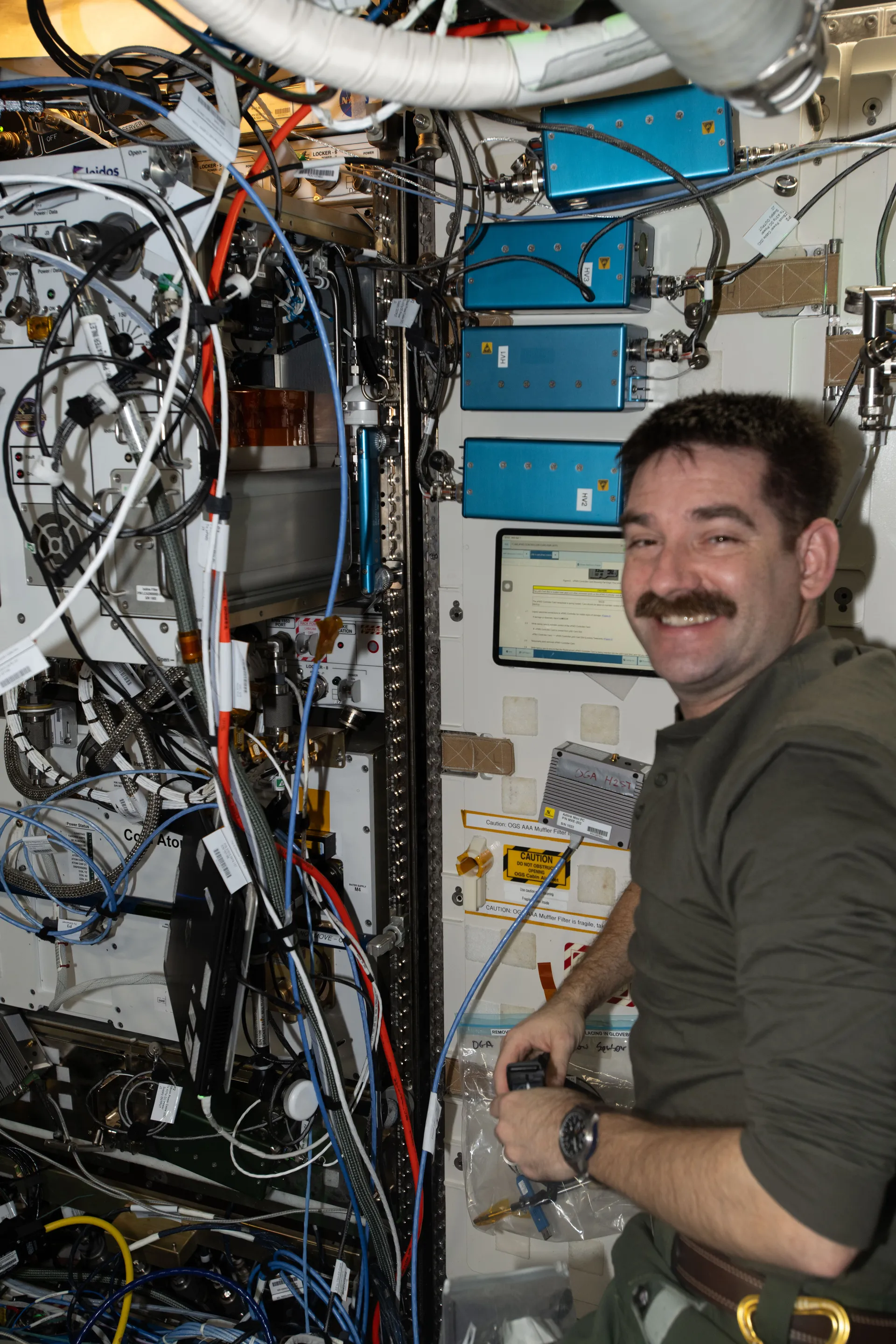 Jack Hathaway smiles beside a rack of cables and equipment in the Destiny laboratory, where he was checking a new drinking-water dispenser.
