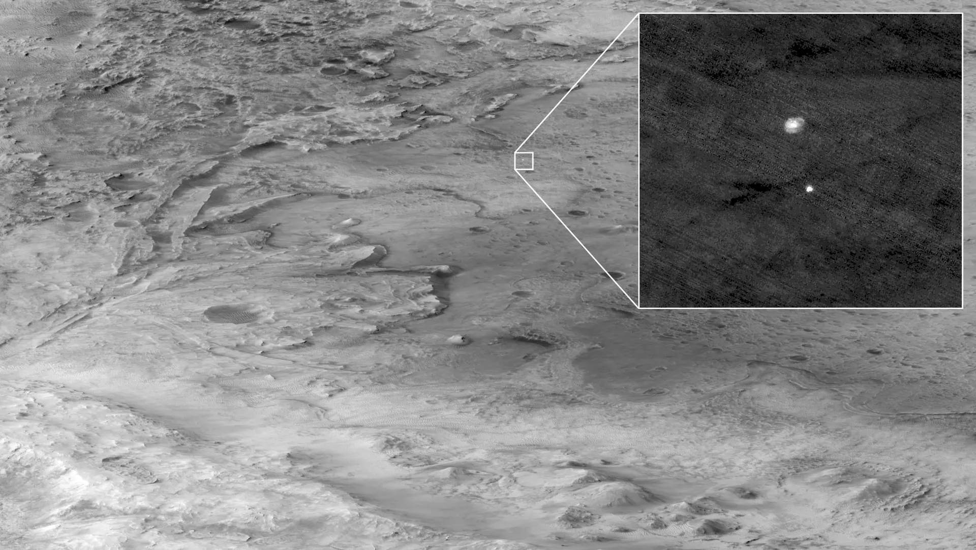 A gray orbital view of a crater floor and an ancient river delta, with an inset showing a tiny parachute and descent stage falling.