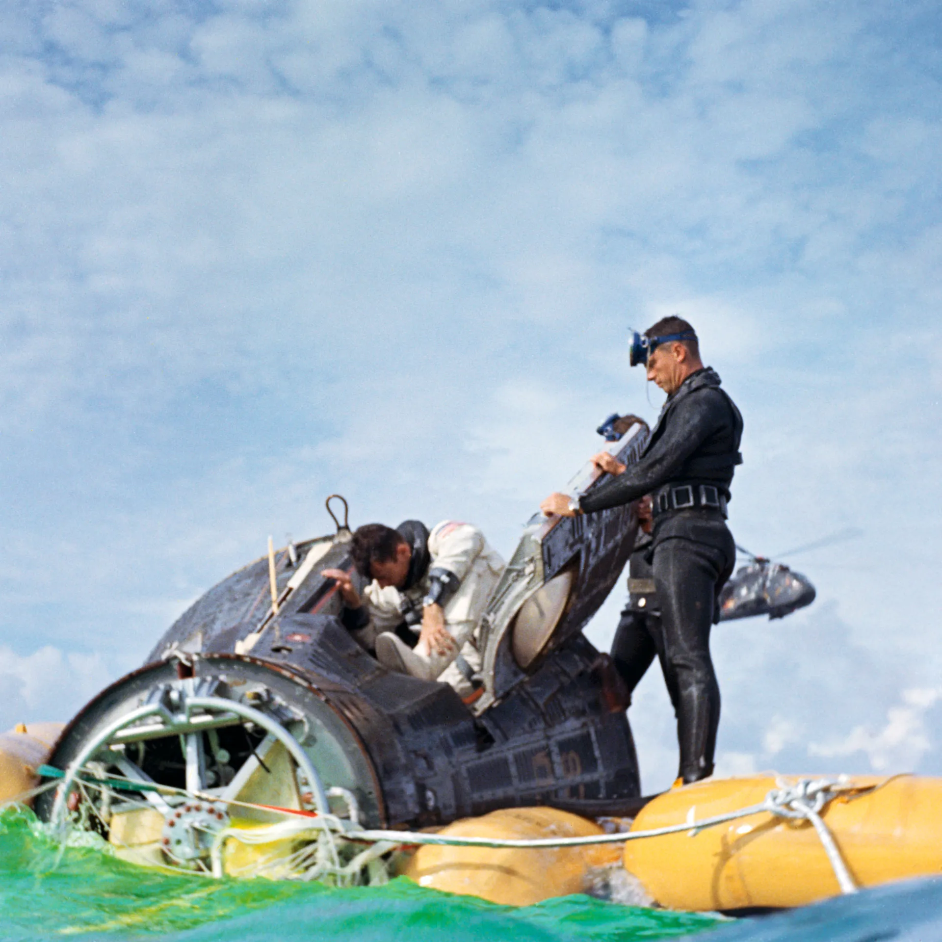 A Navy swimmer on a flotation collar helps John Young climb out of the Gemini 10 capsule.