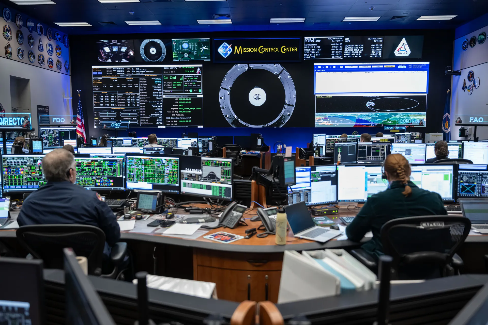 Flight controllers at consoles in Houston’s White Flight Control Room, facing large screens of Orion data.