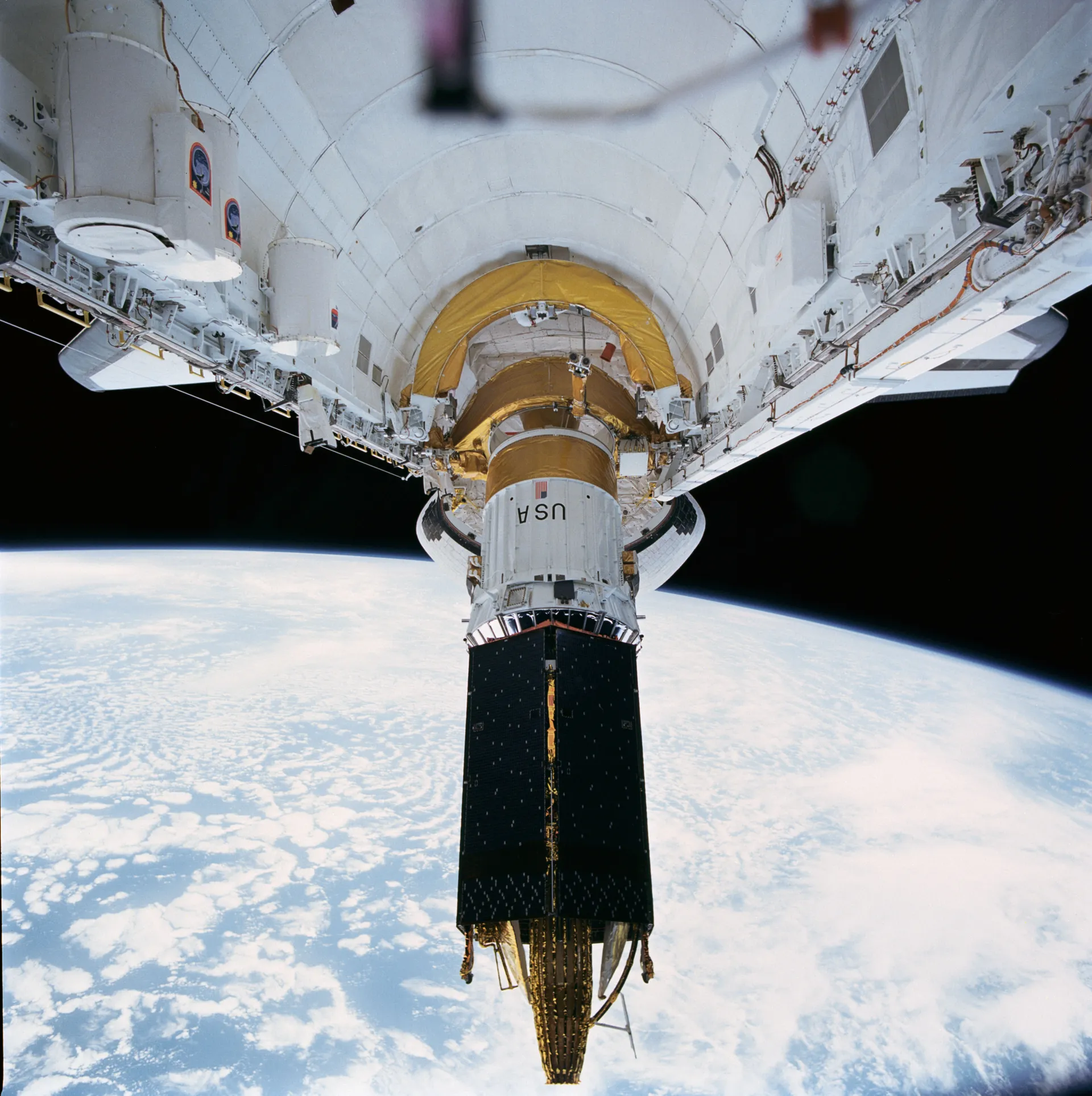 A Tracking and Data Relay Satellite rising out of a Space Shuttle’s payload bay, with Earth below.