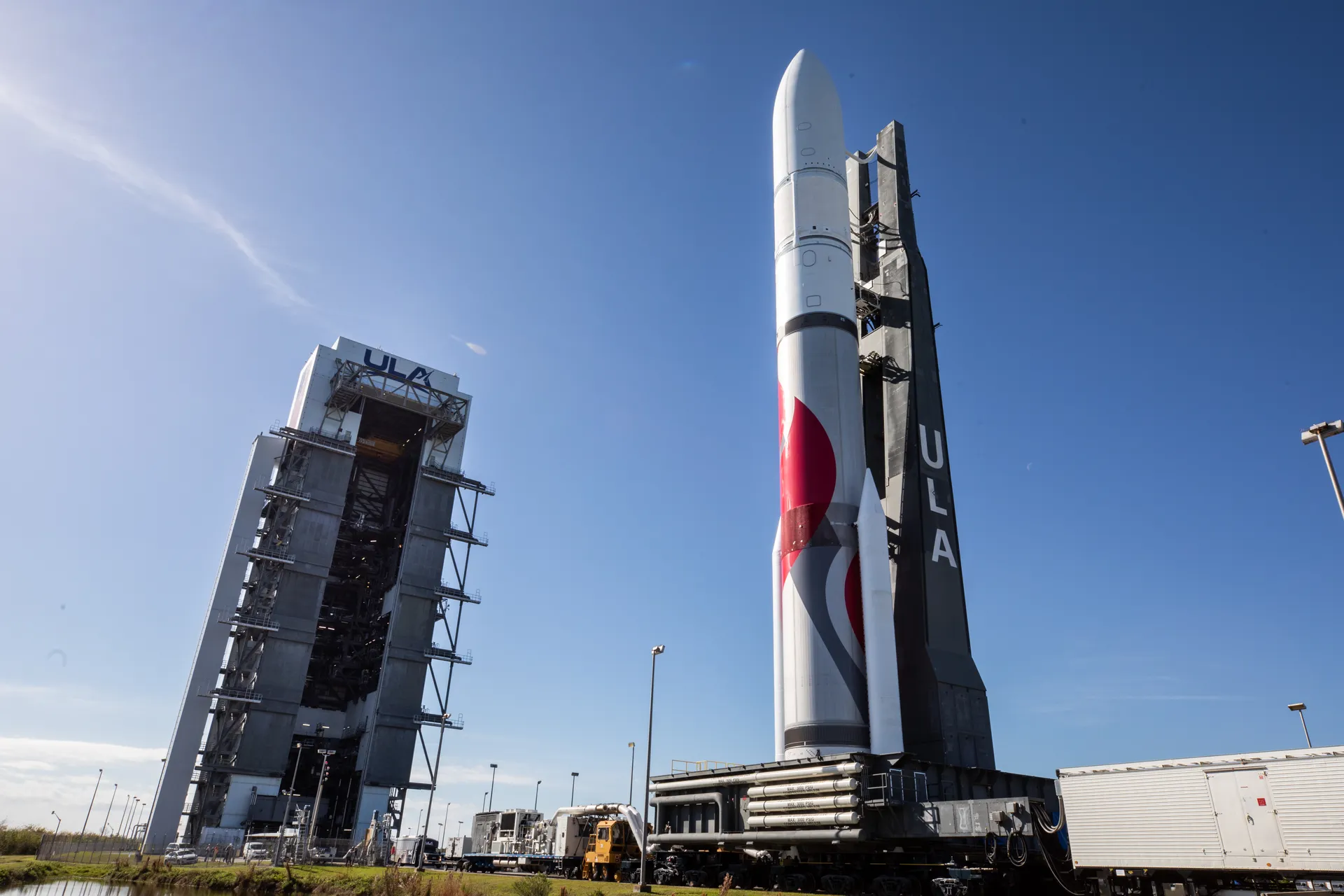 A white and red Vulcan rocket stands on its mobile platform beside the tall Vertical Integration Facility under a blue sky.