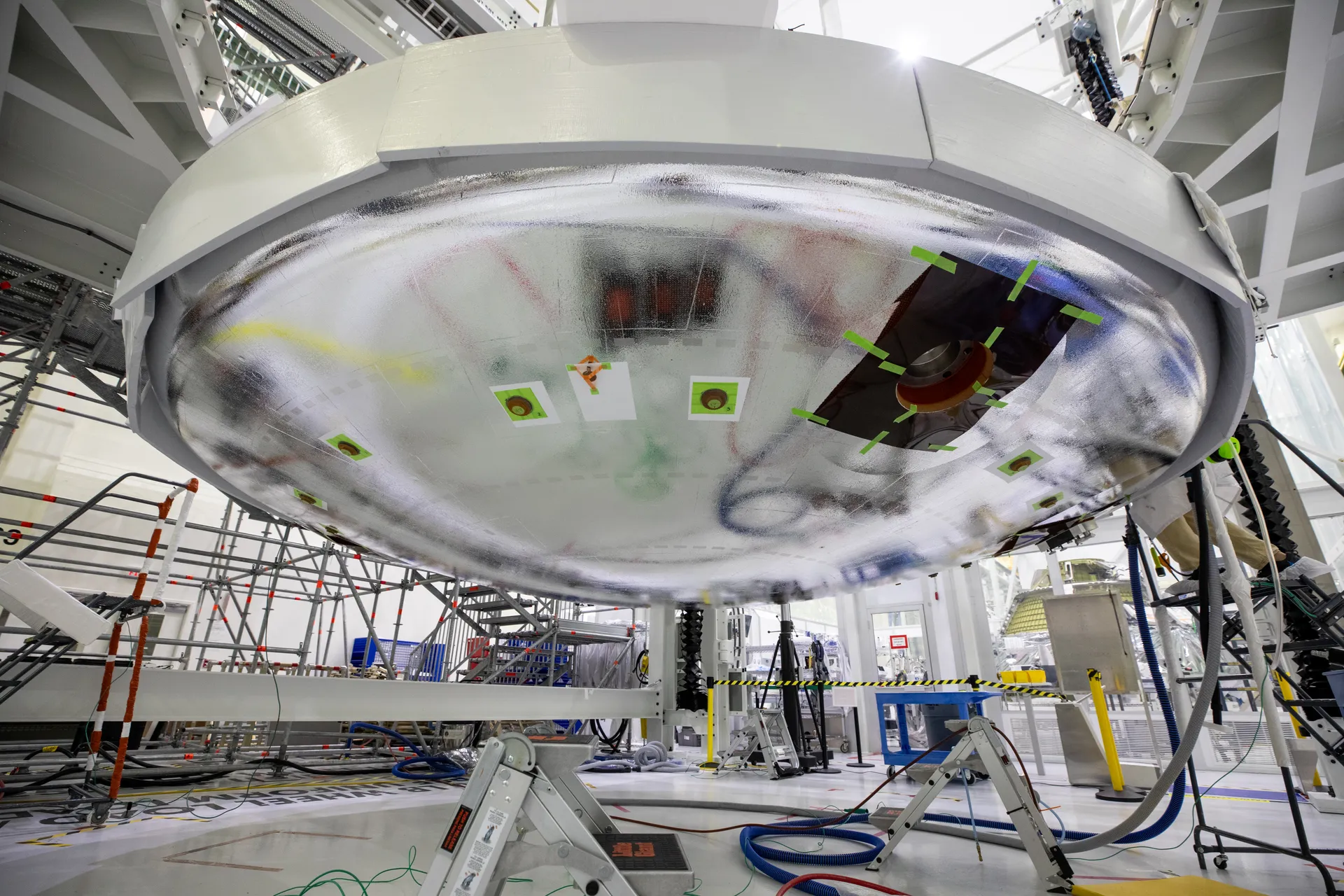 The silver-covered Artemis II heat shield being lifted into place beneath the crew module in a high bay.