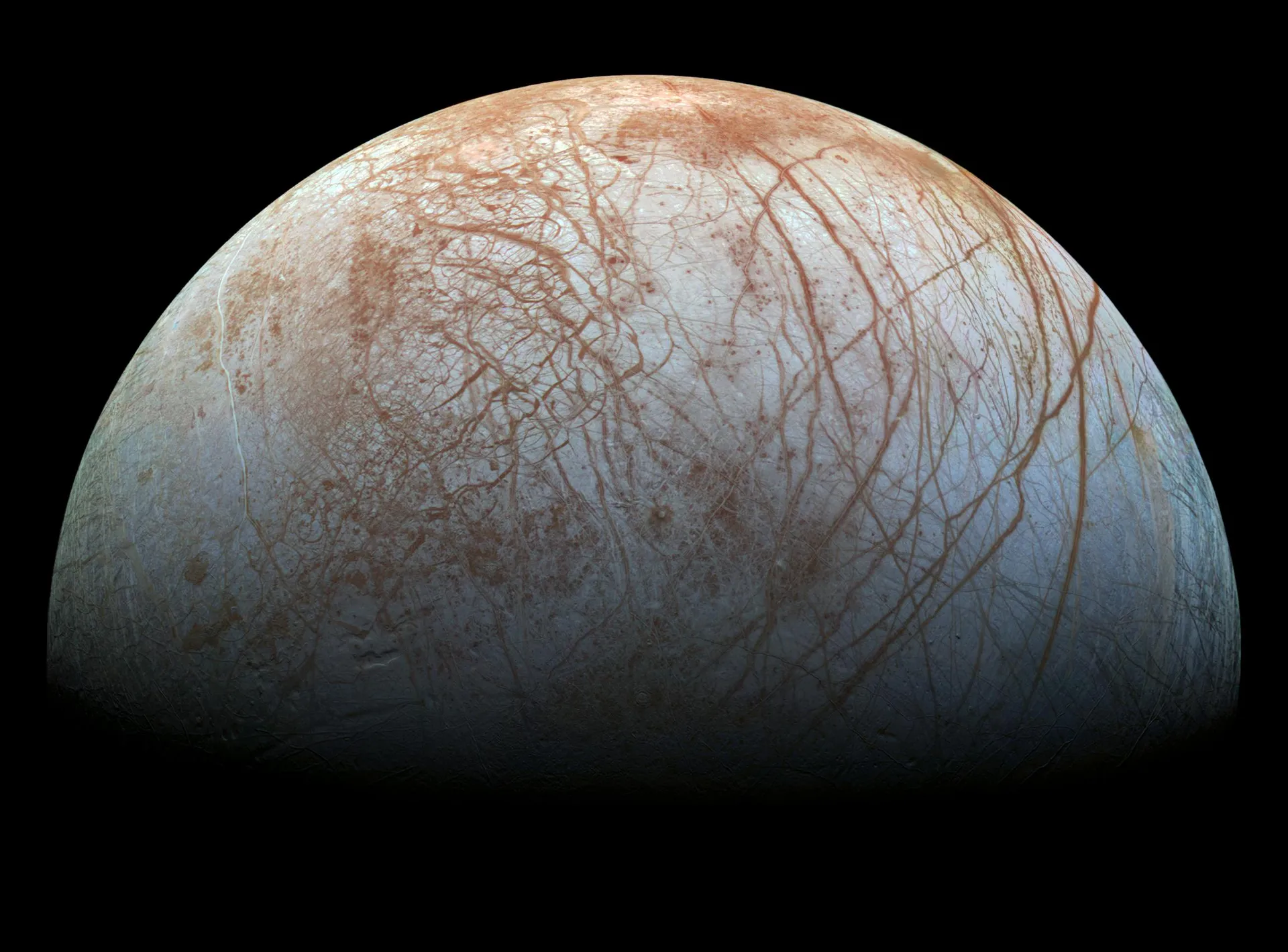 Half of Europa against black space: a white and pale blue icy surface criss-crossed by long reddish-brown cracks and ridges.