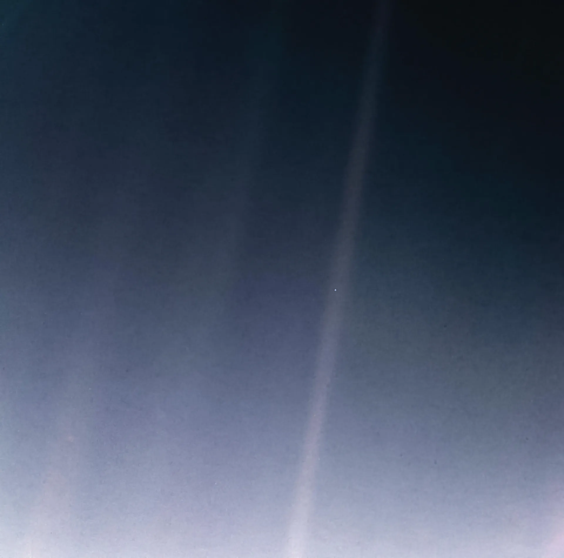 A grainy black field crossed by soft bands of scattered sunlight; within the brightest band, just right of center, is a tiny bluish dot: Earth.