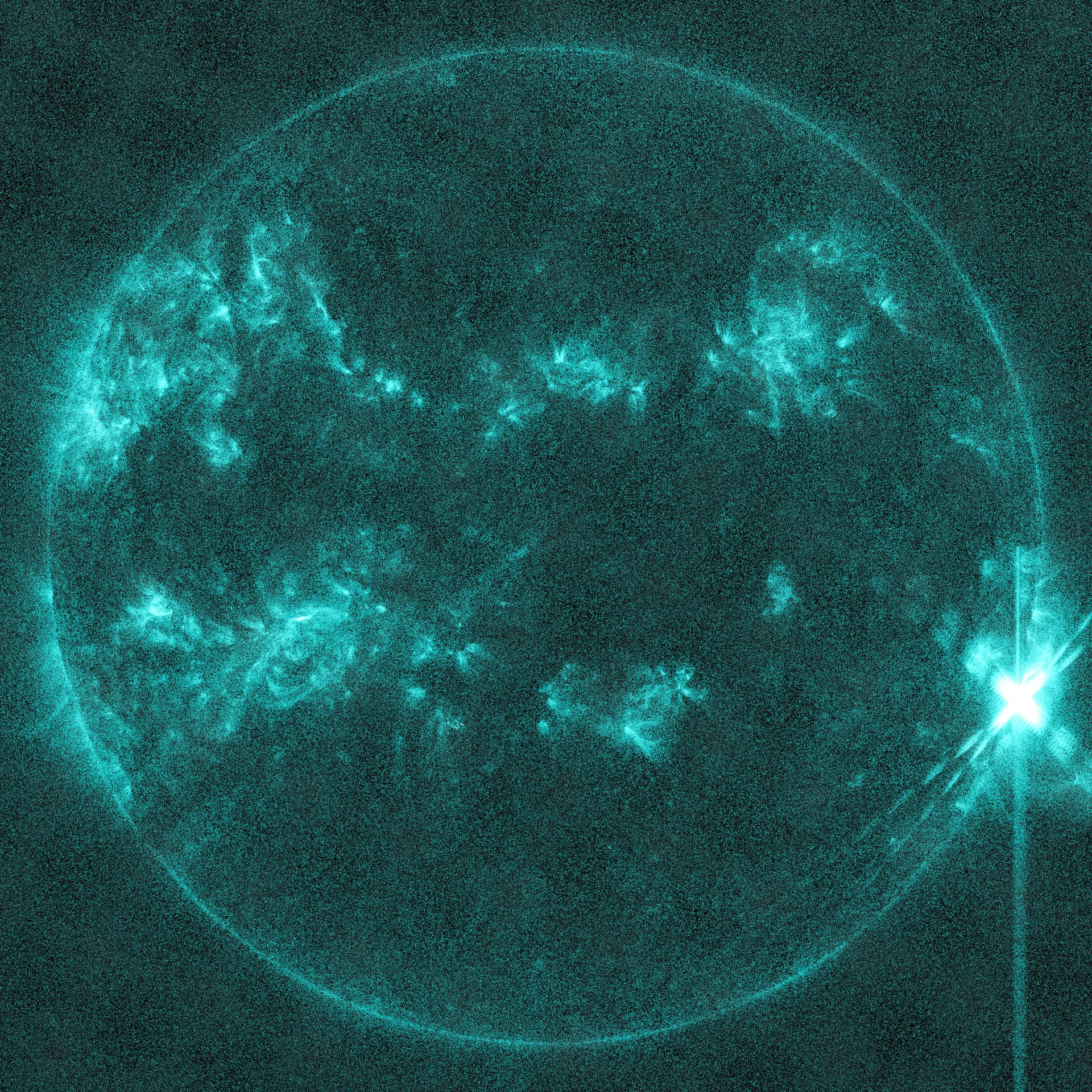 The Sun in teal extreme ultraviolet light with scattered bright regions and an intense white flash on its right edge, with diffraction streaks.