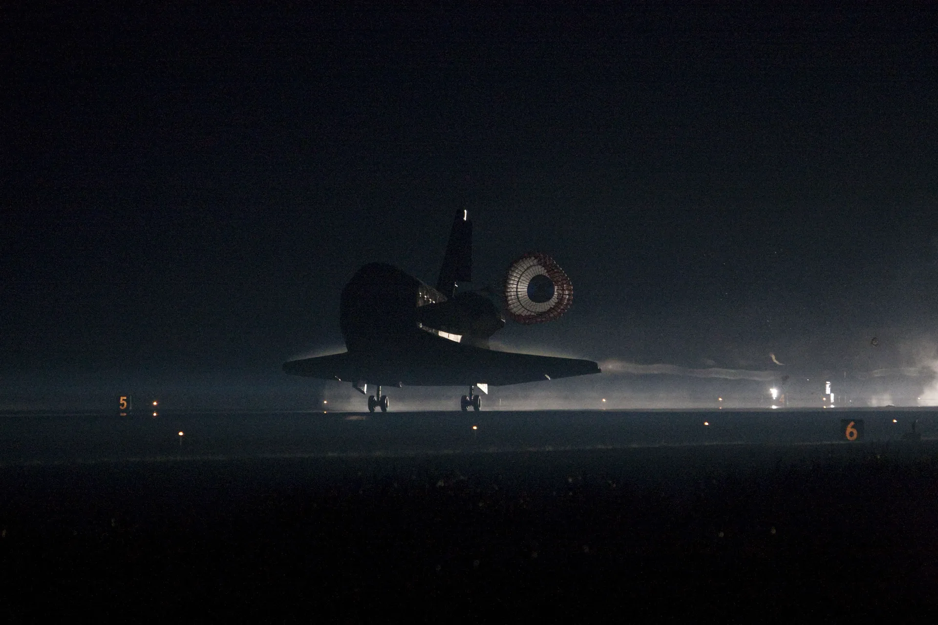 Atlantis rolls down the runway in the dark before sunrise with its drag chute deployed.