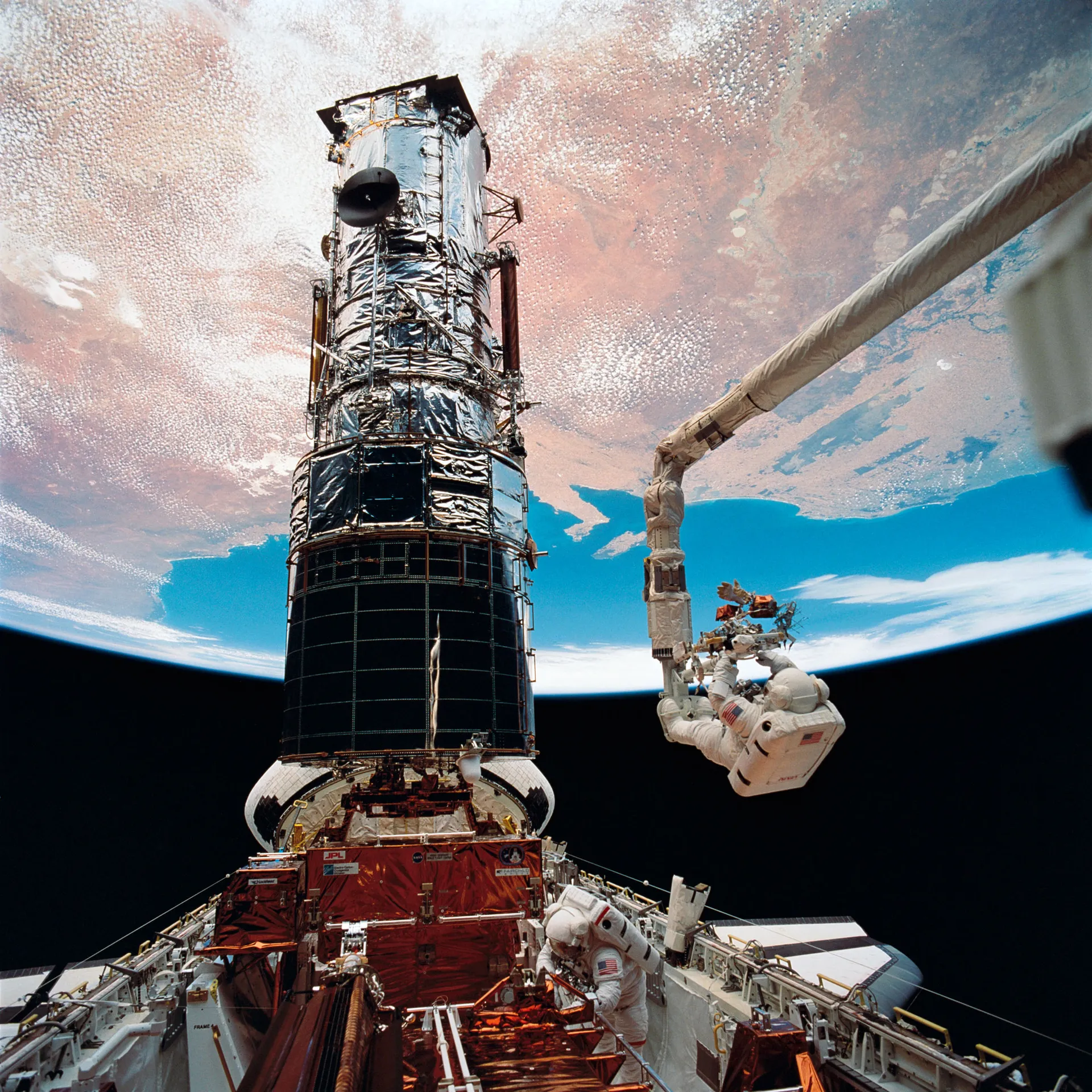 An astronaut on the end of the robotic arm beside the Hubble telescope, above Endeavour’s cargo bay and Earth.